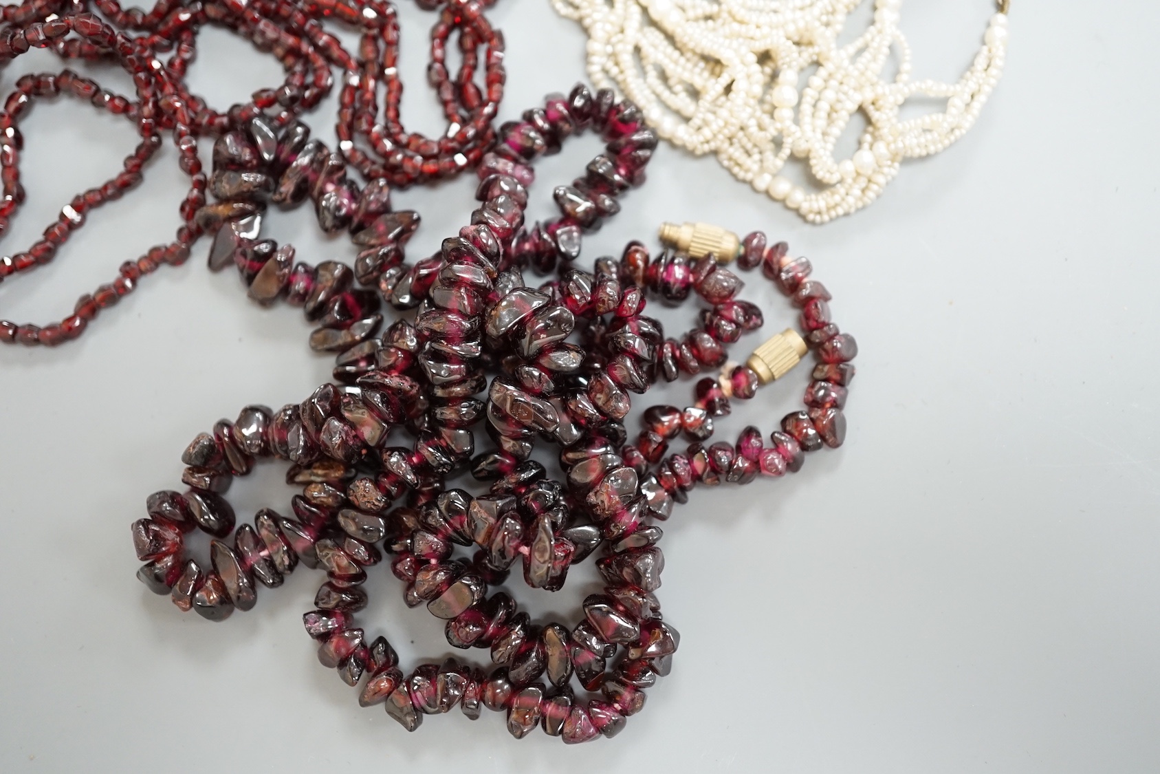 An early 20th century triple strand facet cut garnet necklace, with yellow metal clasp, 122cm, a similar single strand garnet 'pebble' necklace and a seed pearl necklace, 118cm.